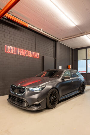 Getunter schwarzer Sportwagen in Garage mit Neonschrift.